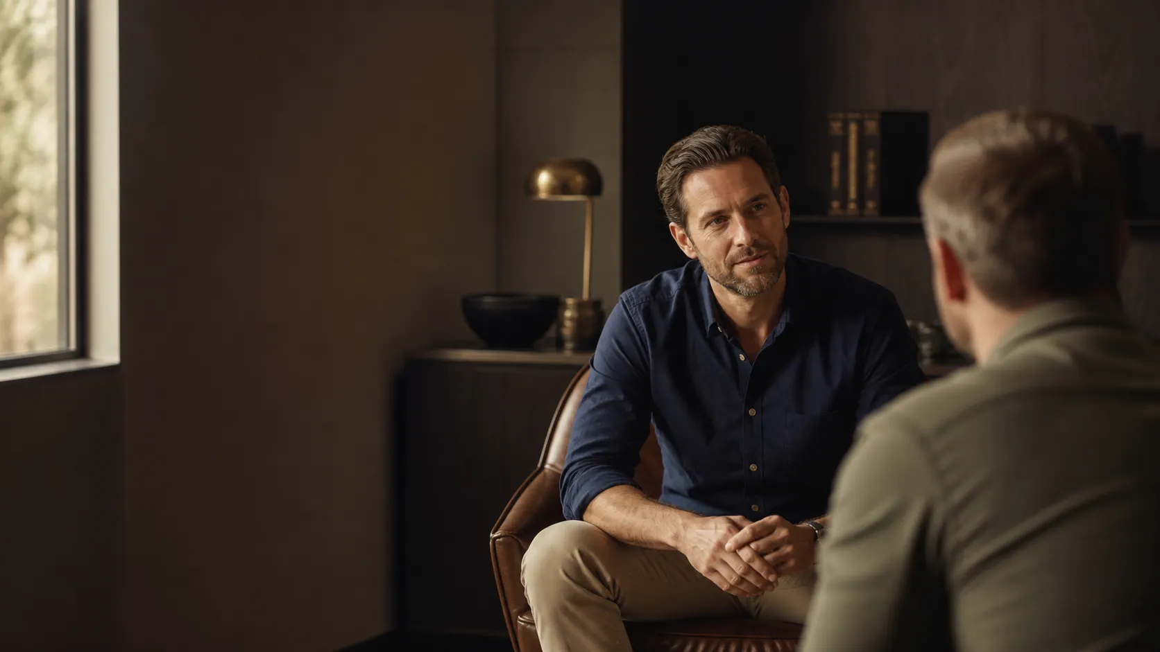 Practitioner and patient meet in a dark-wood men's health consultation room.