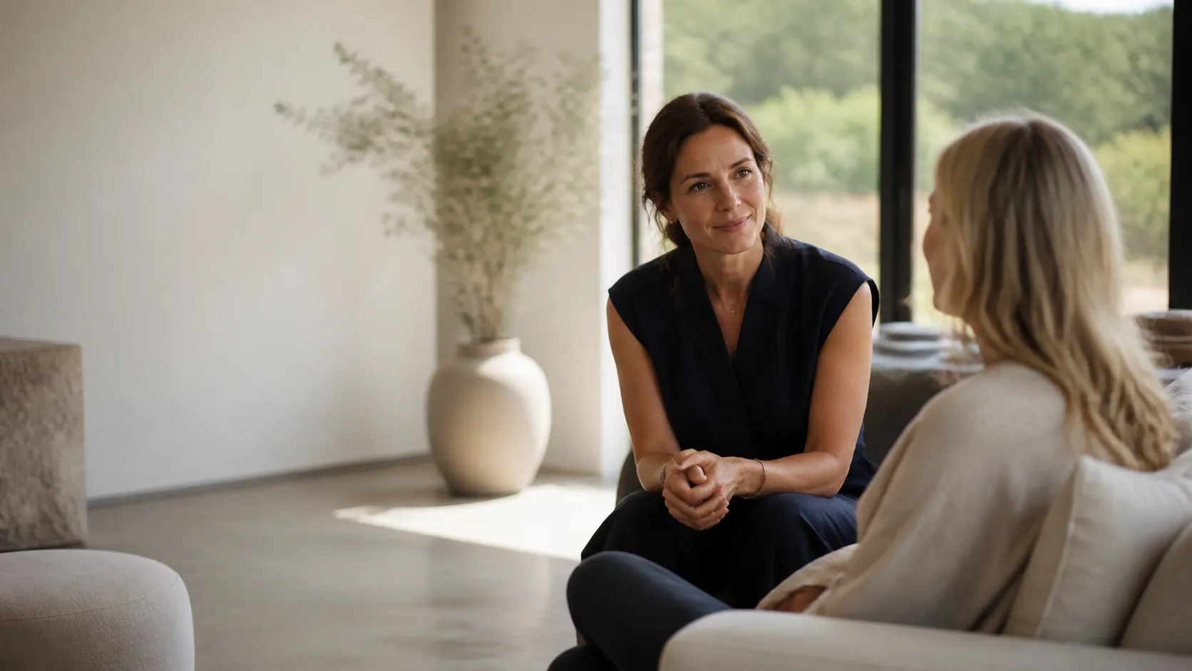 Practitioner and patient meet in a bright wellness studio with stone, linen, and greenery.